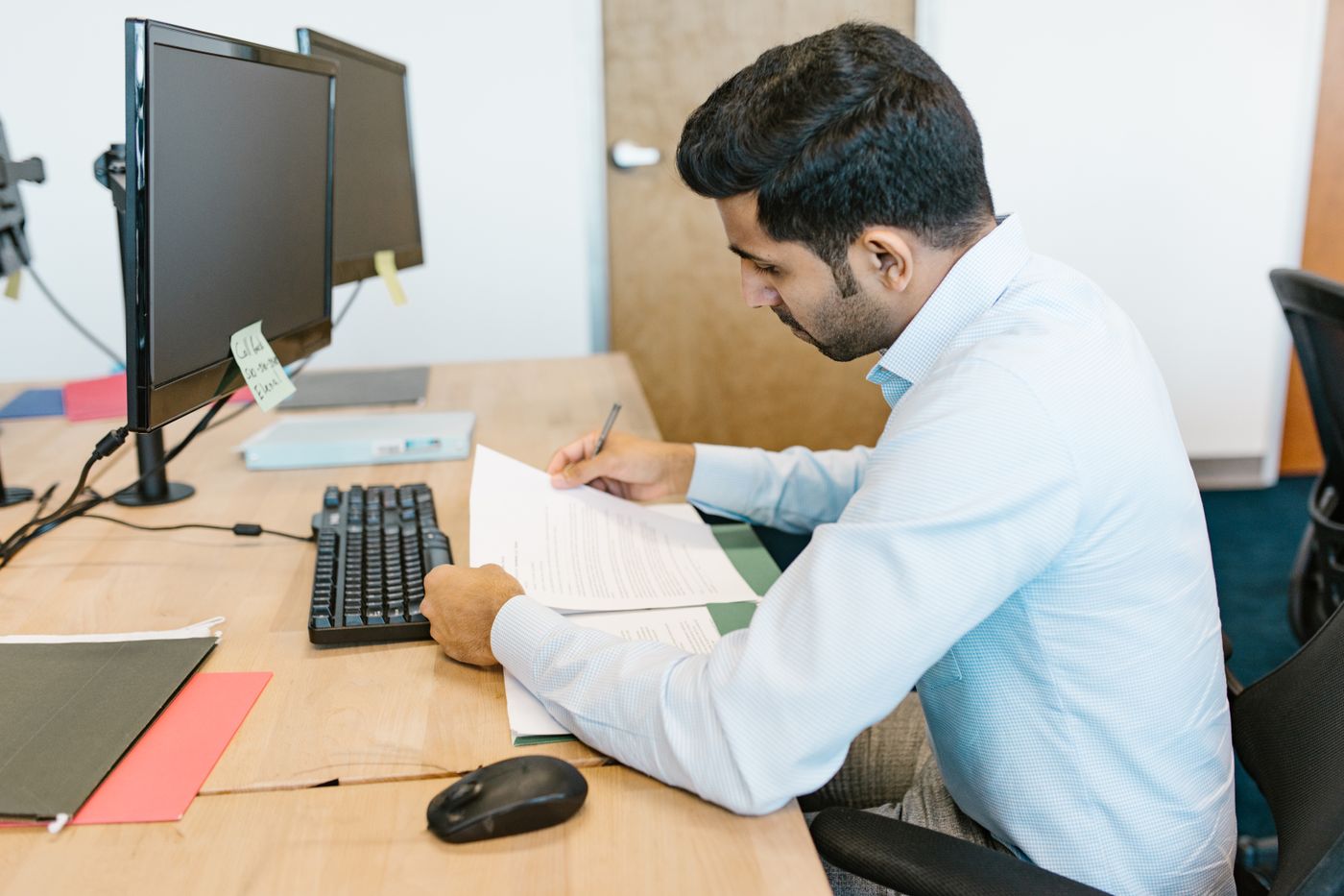 A payments officer reviewing documents at a desk with two monitors